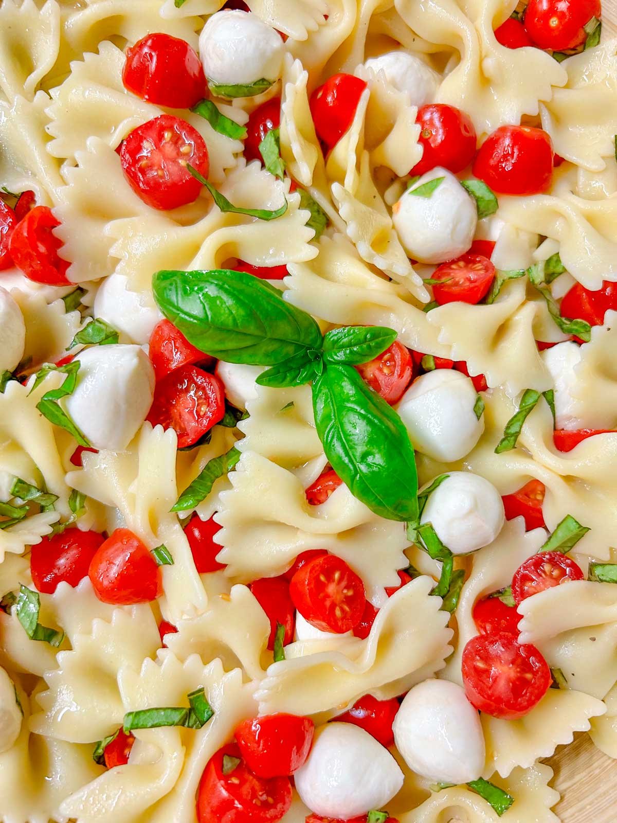 a wooden bowl is filled with caprese pasta salad and garnished with fresh basil