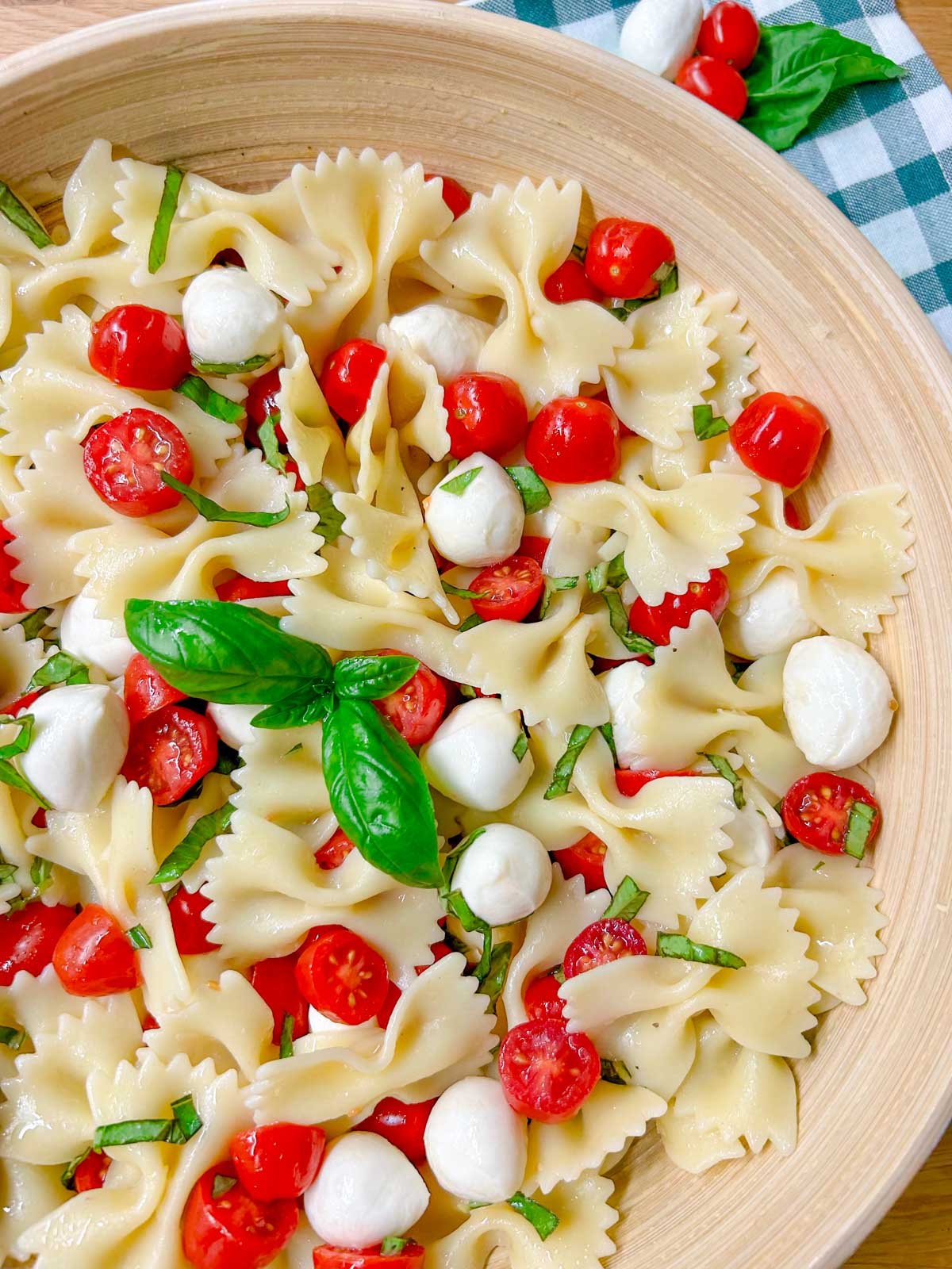 a wooden bowl is filled with caprese pasta salad and garnished with fresh basil