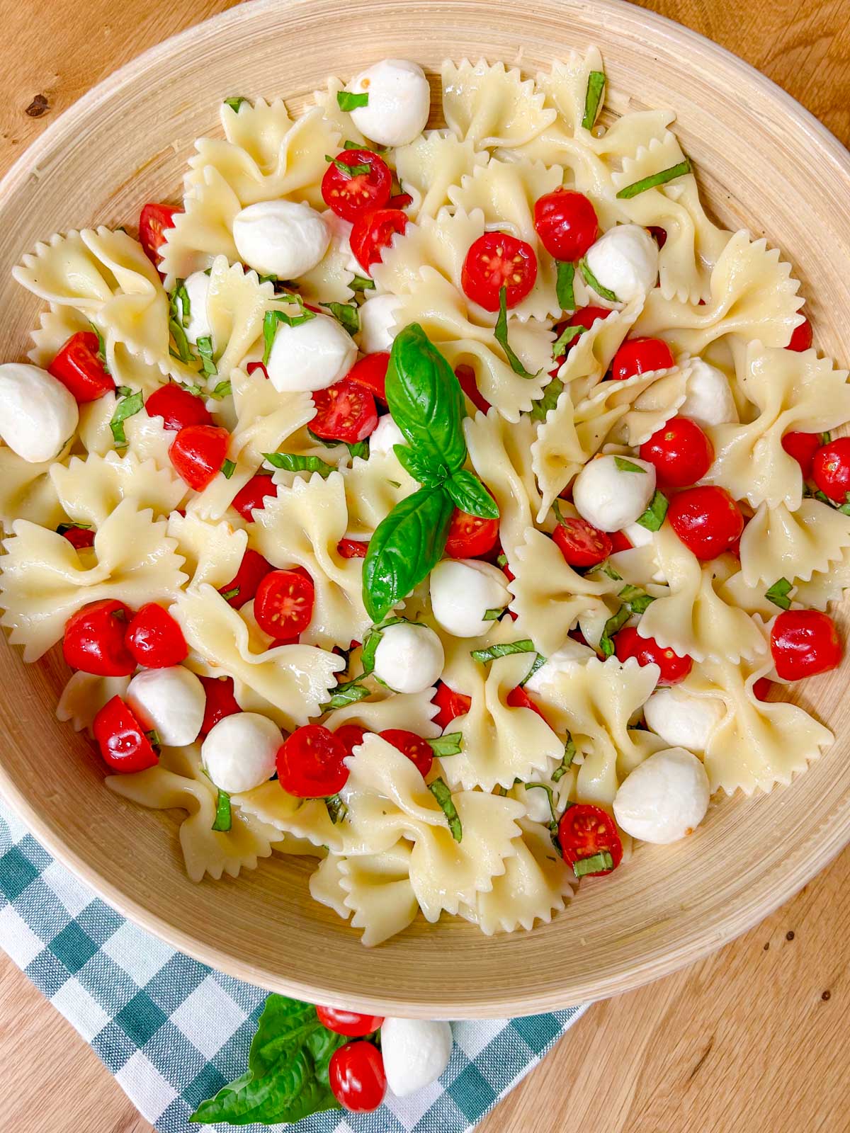 a wooden bowl is filled with caprese pasta salad and garnished with fresh basil