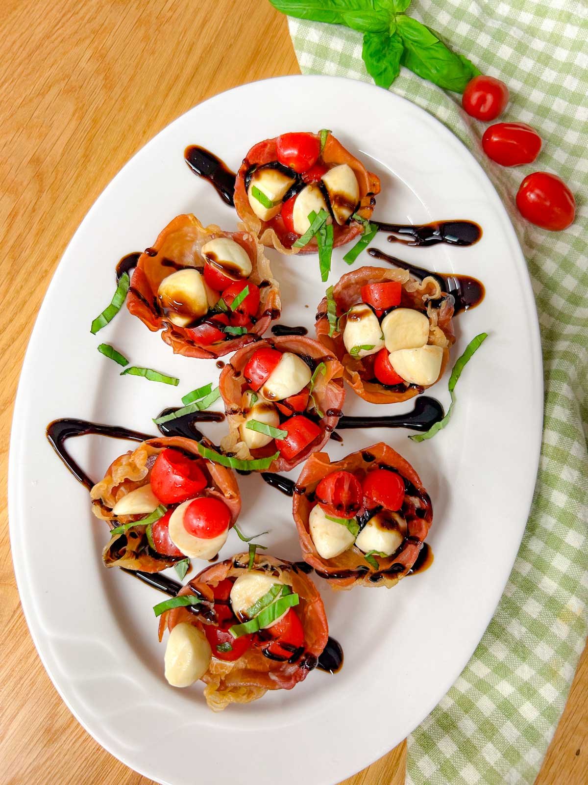 a white platter has crispy caprese prosciutto cups with balsamic glaze drizzled over top.