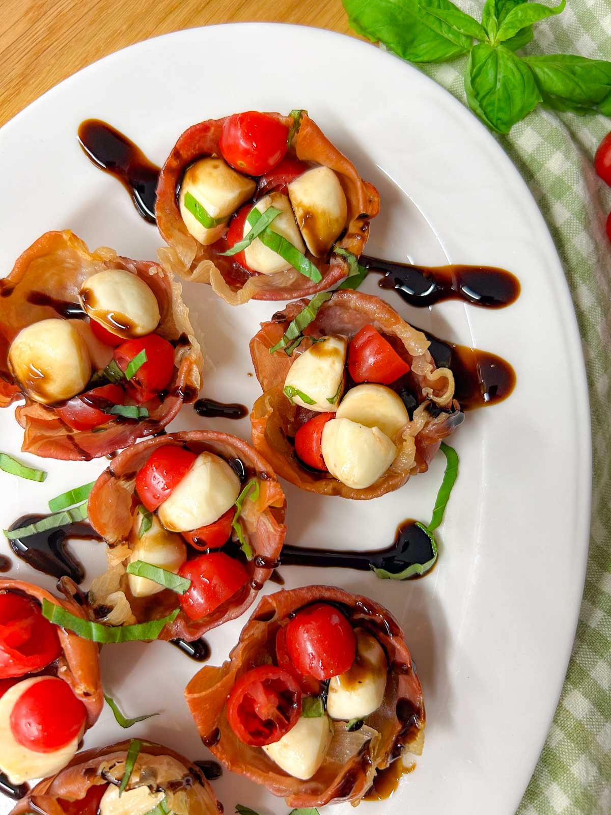 a white platter has crispy caprese prosciutto cups with balsamic glaze drizzled over top.