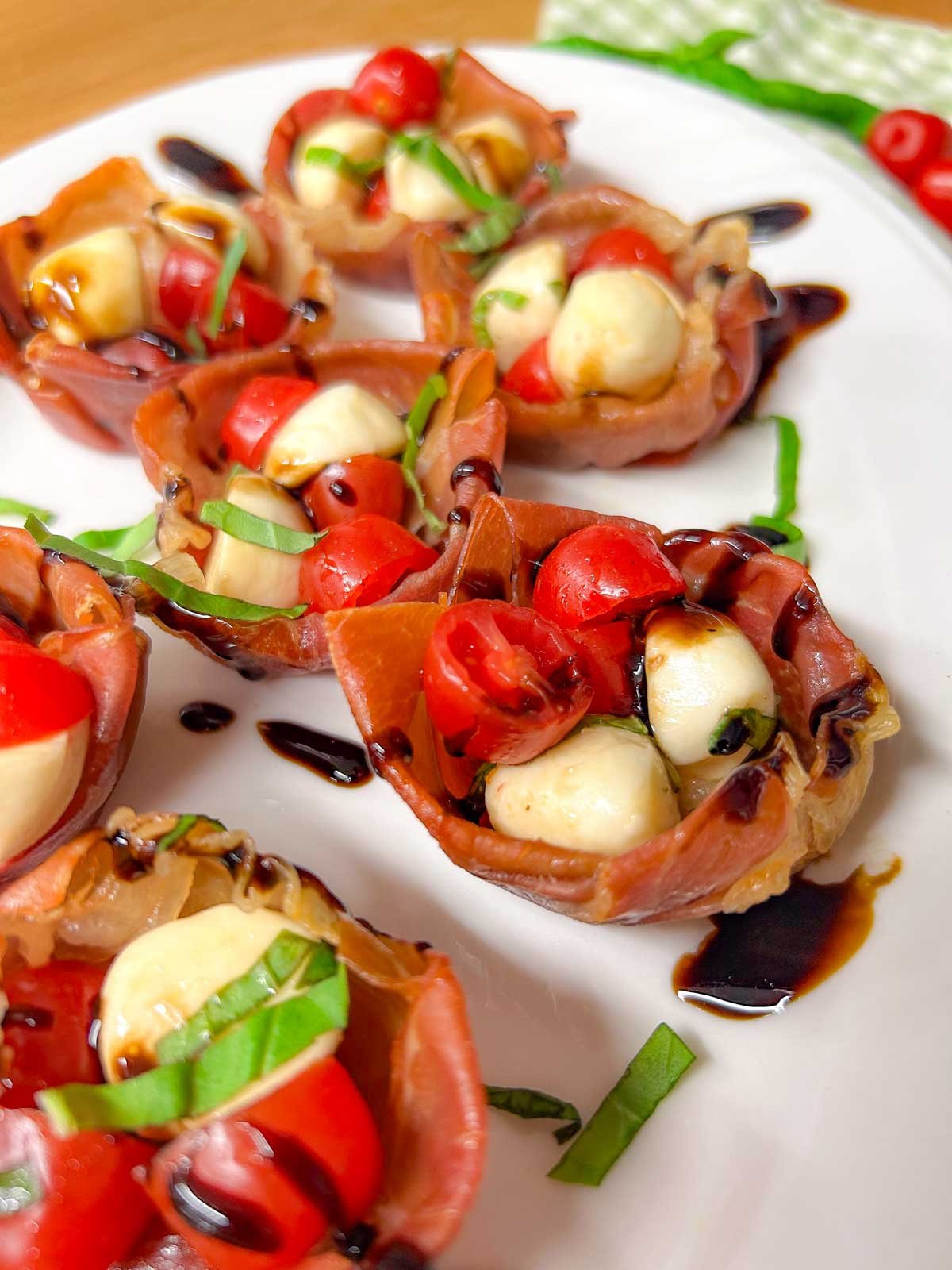 a white platter has crispy caprese prosciutto cups with balsamic glaze drizzled over top.