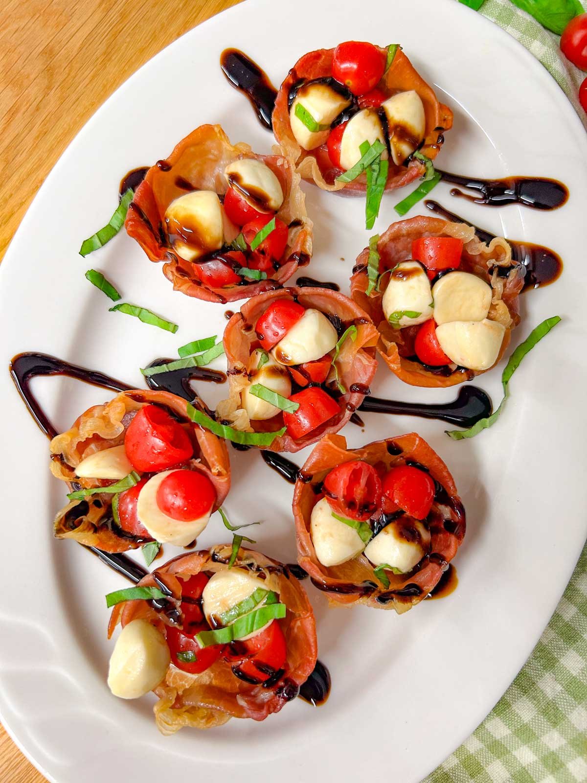 a white platter has crispy caprese prosciutto cups with balsamic glaze drizzled over top.