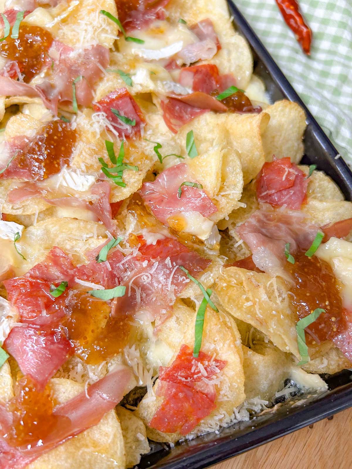 a black rimmed sheet pan is filled with baked charcuterie nachos and garnished with parmesan cheese and sliced basil.