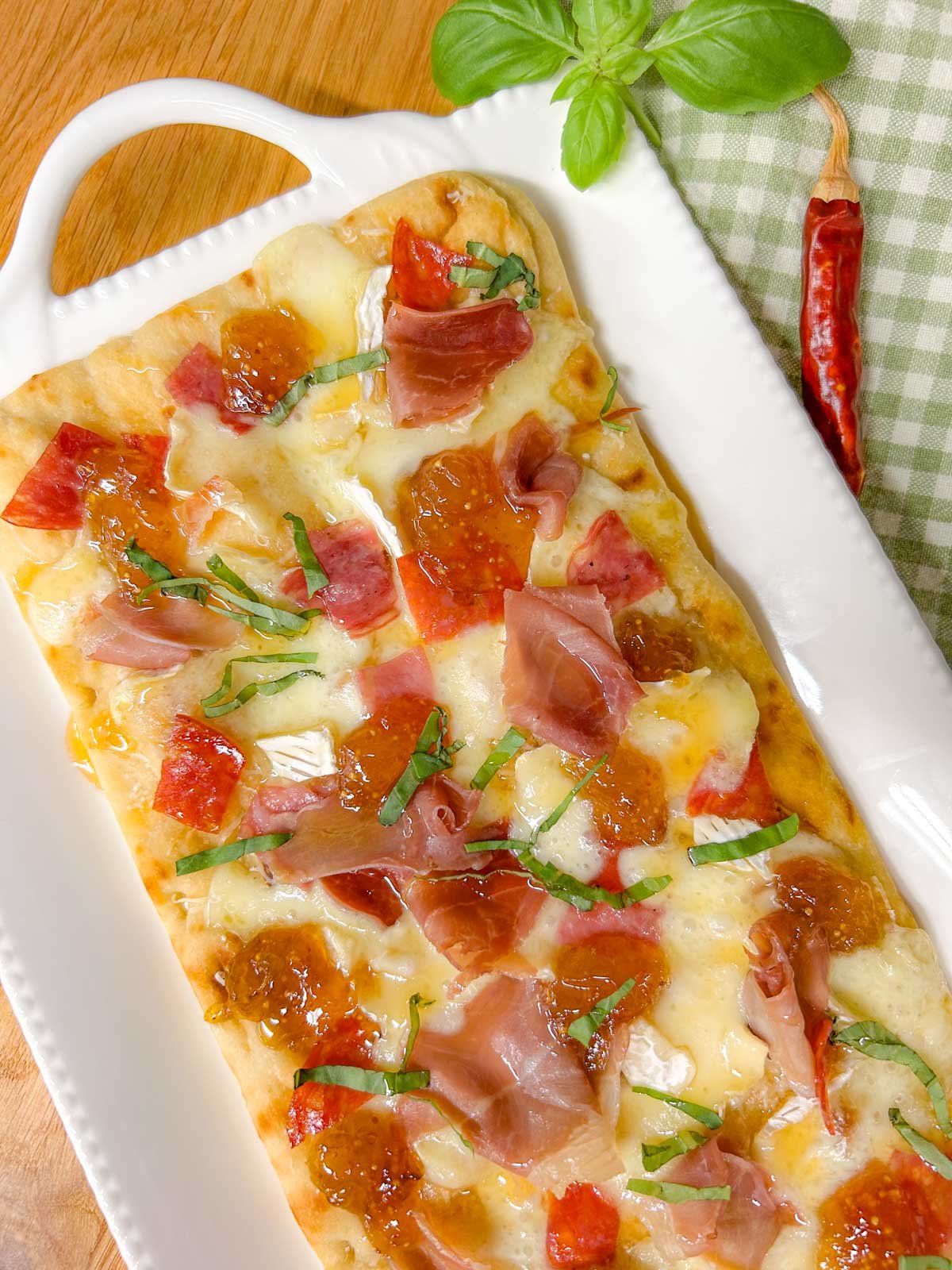 a white platter has a charcuterie flatbread on top that is garnished with thinly sliced basil.