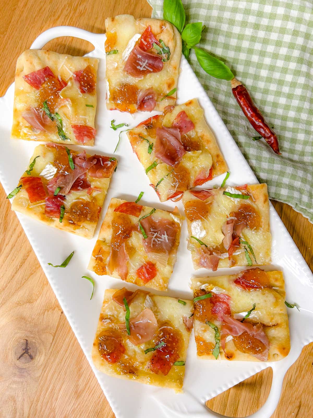 a white platter has a charcuterie flatbread on top that is garnished with thinly sliced basil.