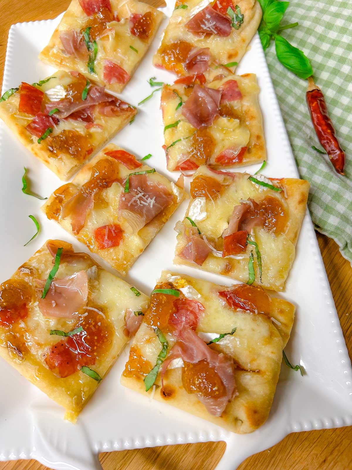 a white platter has a charcuterie flatbread on top that is garnished with thinly sliced basil.