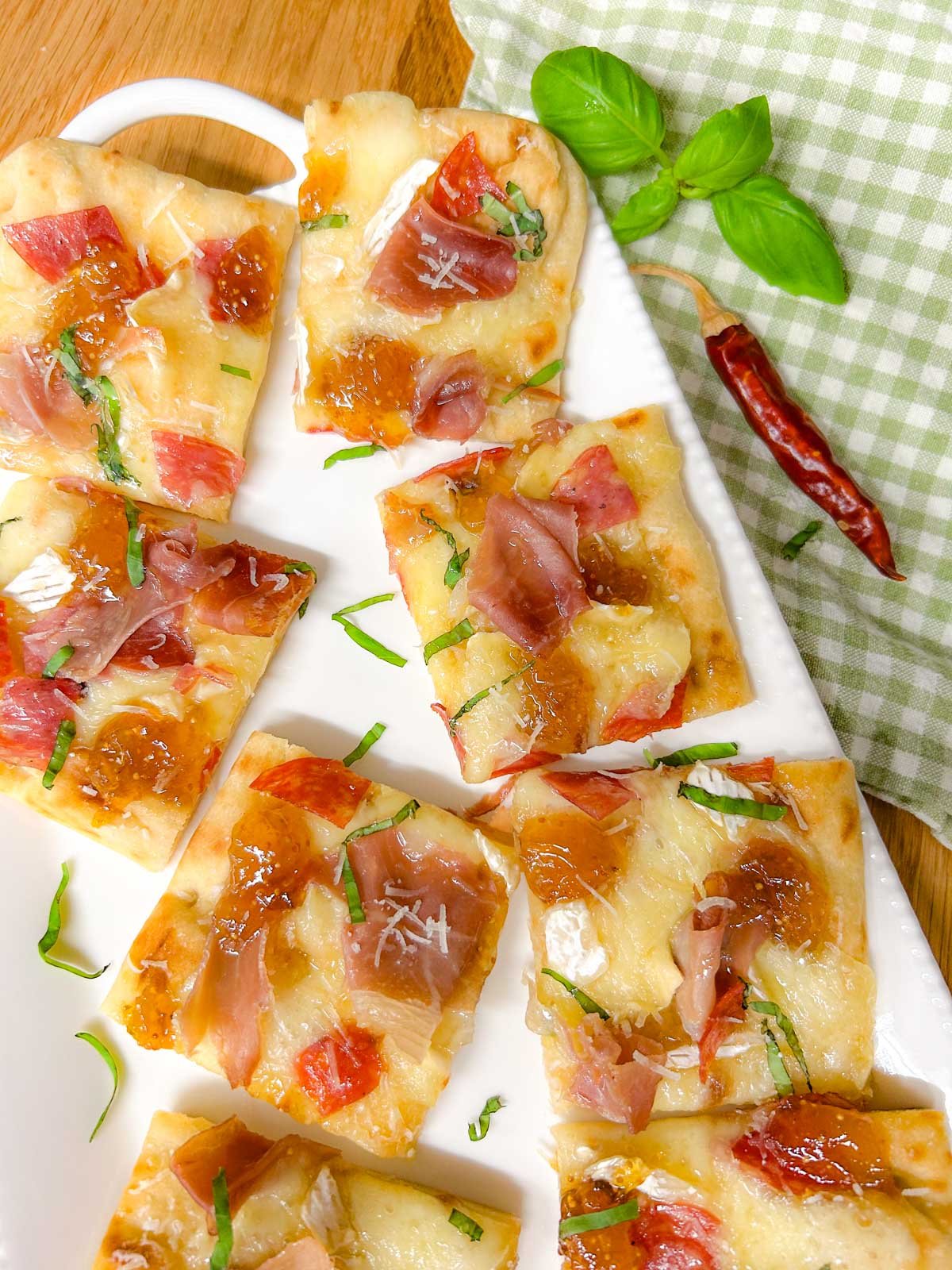a white platter has a charcuterie flatbread on top that is garnished with thinly sliced basil.