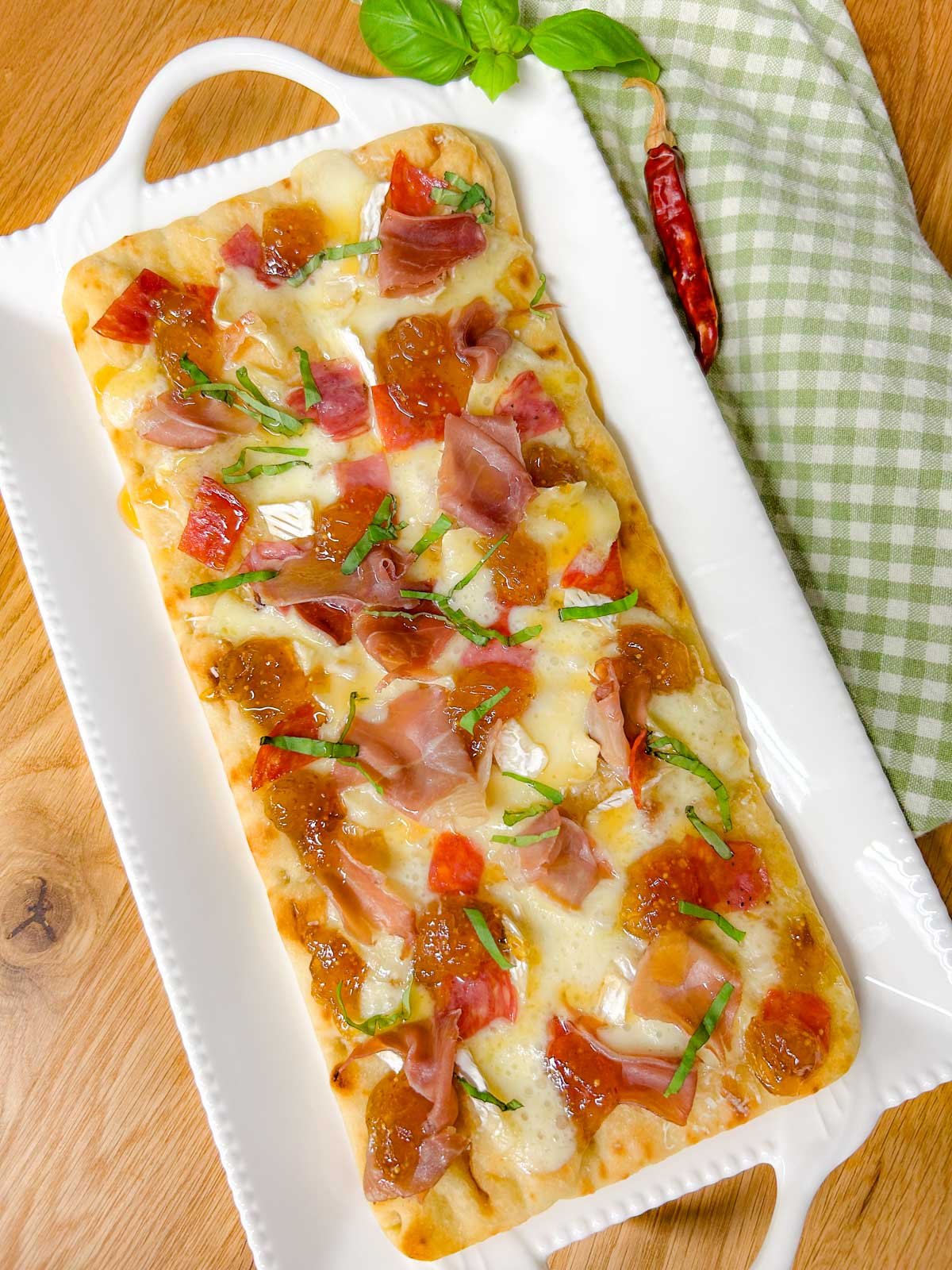 a white platter has a charcuterie flatbread on top that is garnished with thinly sliced basil.