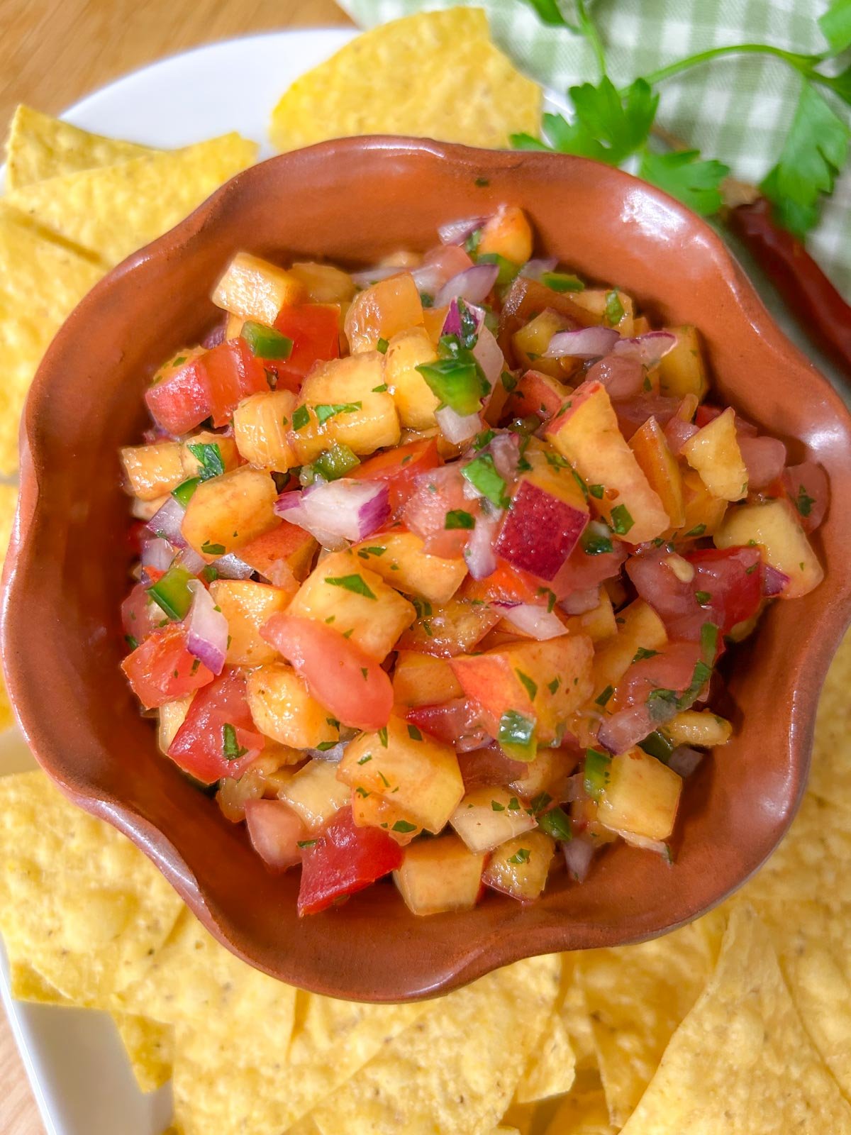 a bowl of chipotle peach salsa is served on a platter with tortilla chips.