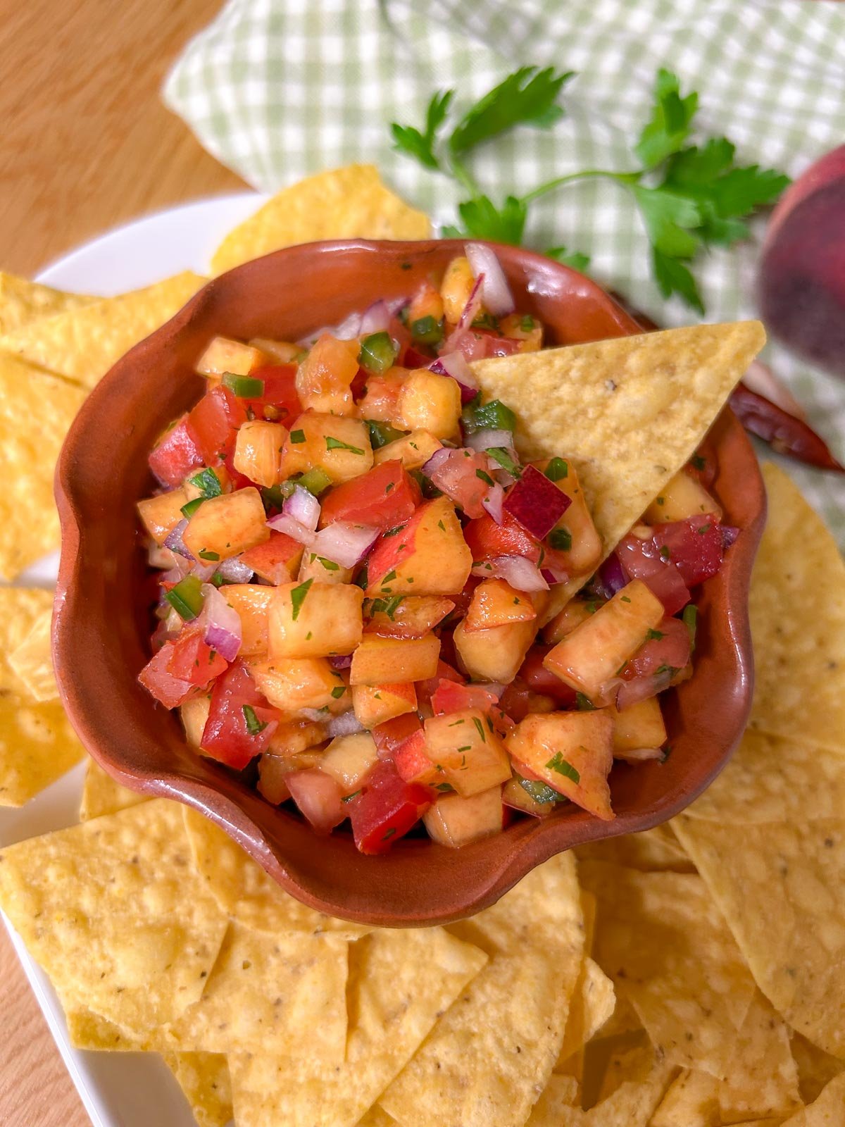 a bowl of chipotle peach salsa is served on a platter with tortilla chips.
