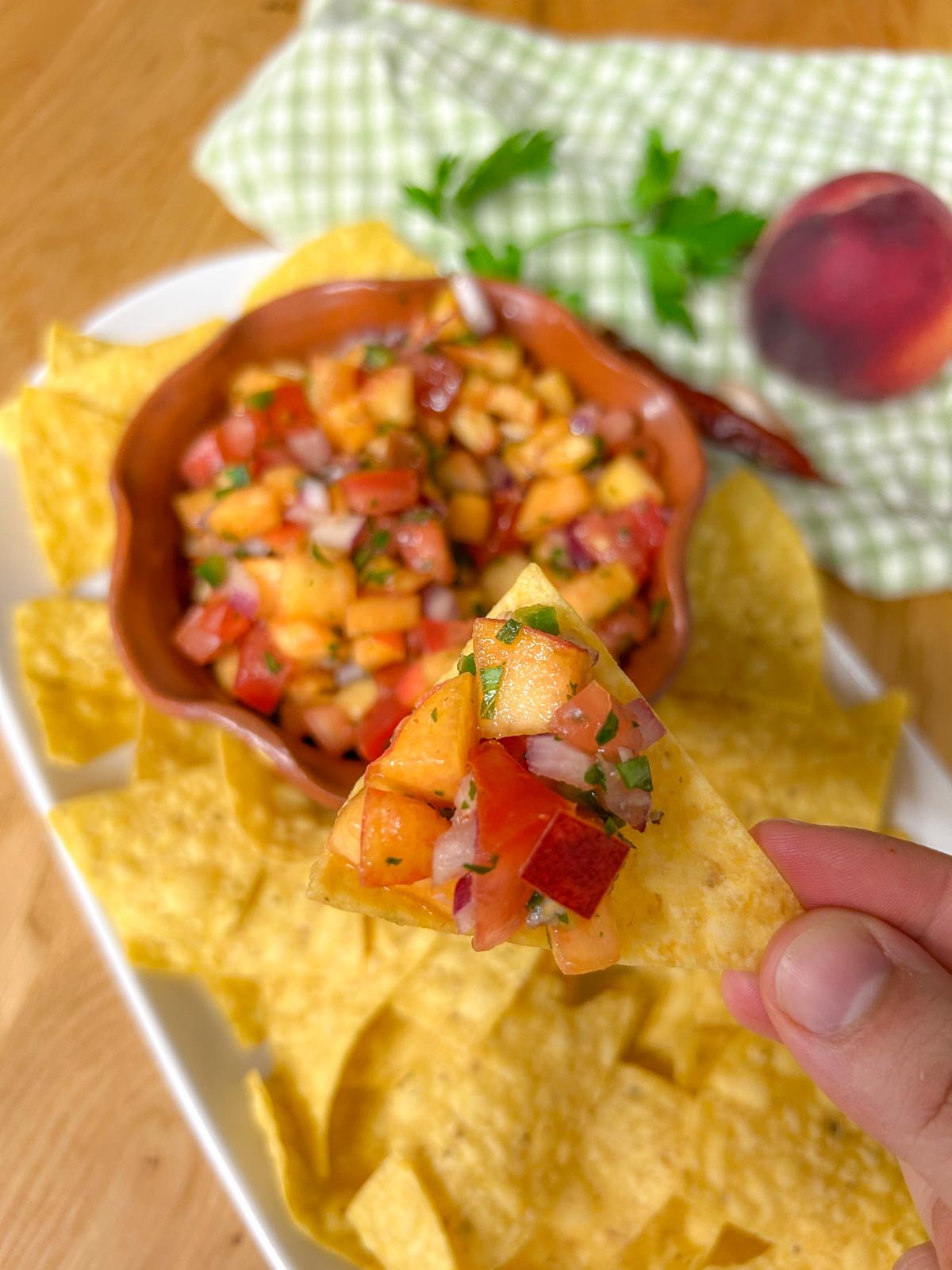 a bowl of chipotle peach salsa is served on a platter with tortilla chips. a chip is dipped in the salsa and held close to the camera.