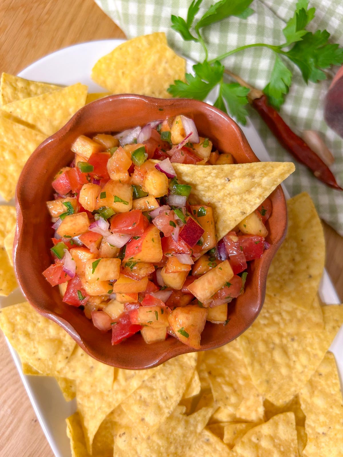 a bowl of chipotle peach salsa is served on a platter with tortilla chips.