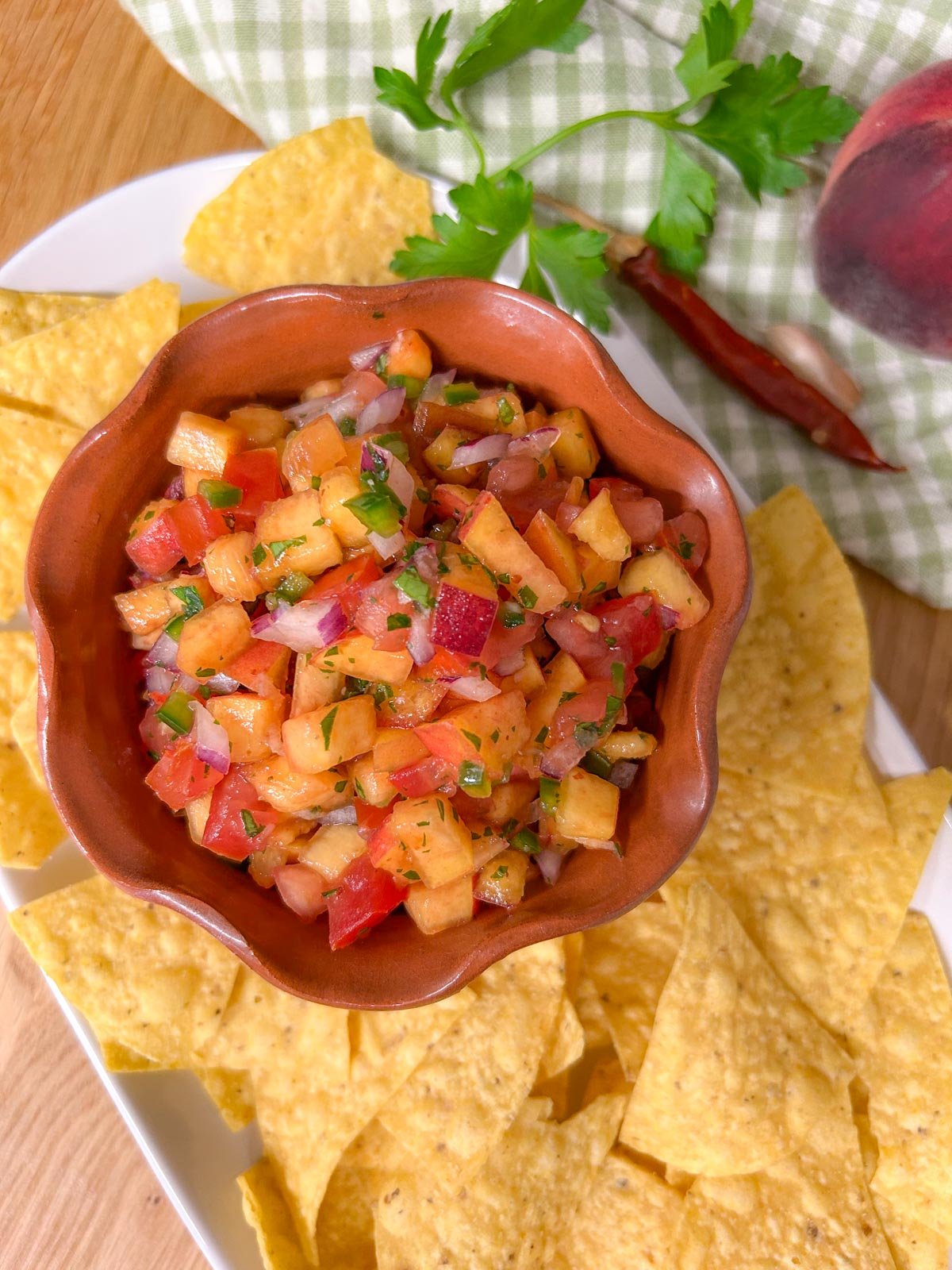 a bowl of chipotle peach salsa is served on a platter with tortilla chips.