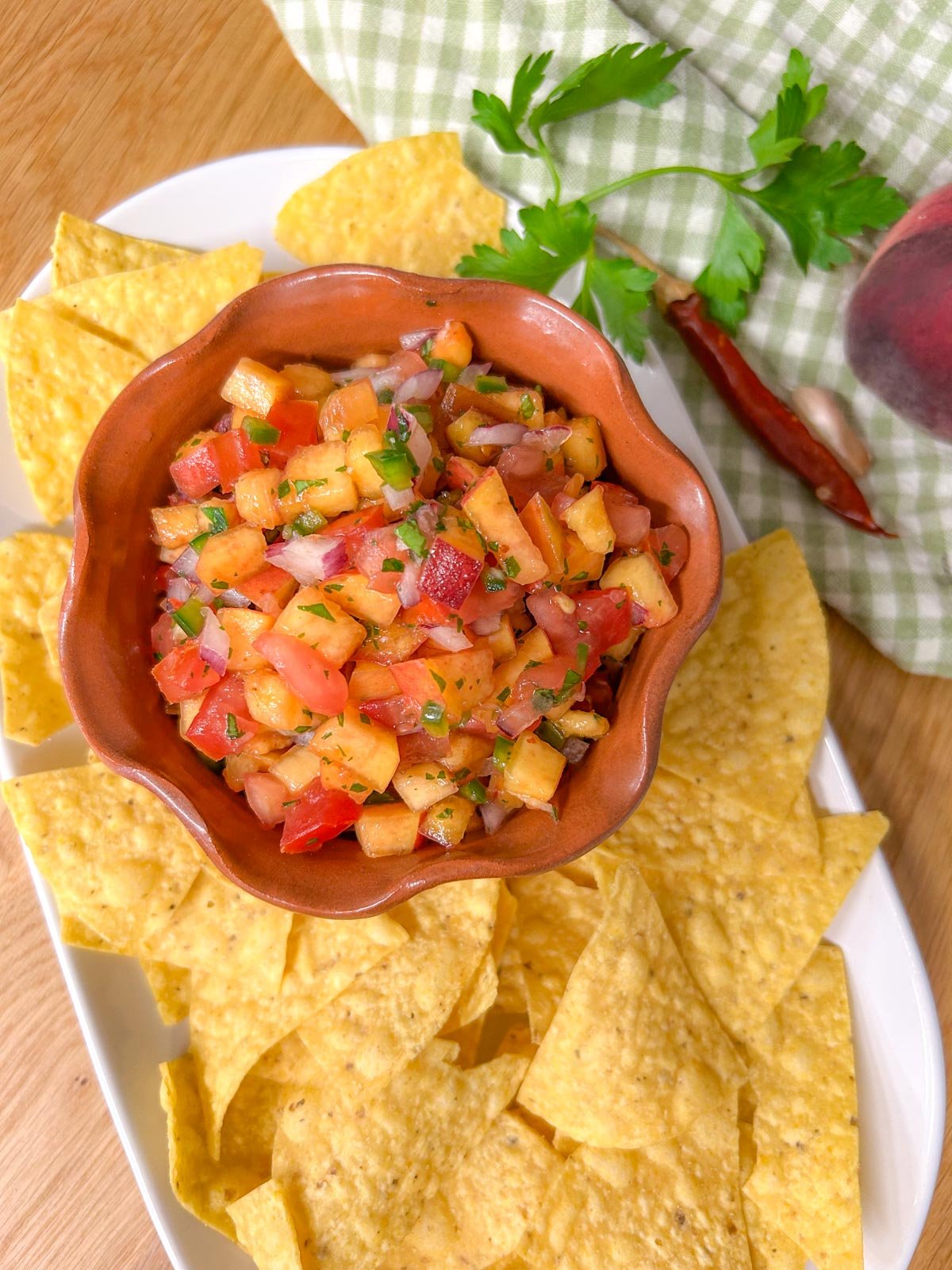 a bowl of chipotle peach salsa is served on a platter with tortilla chips.