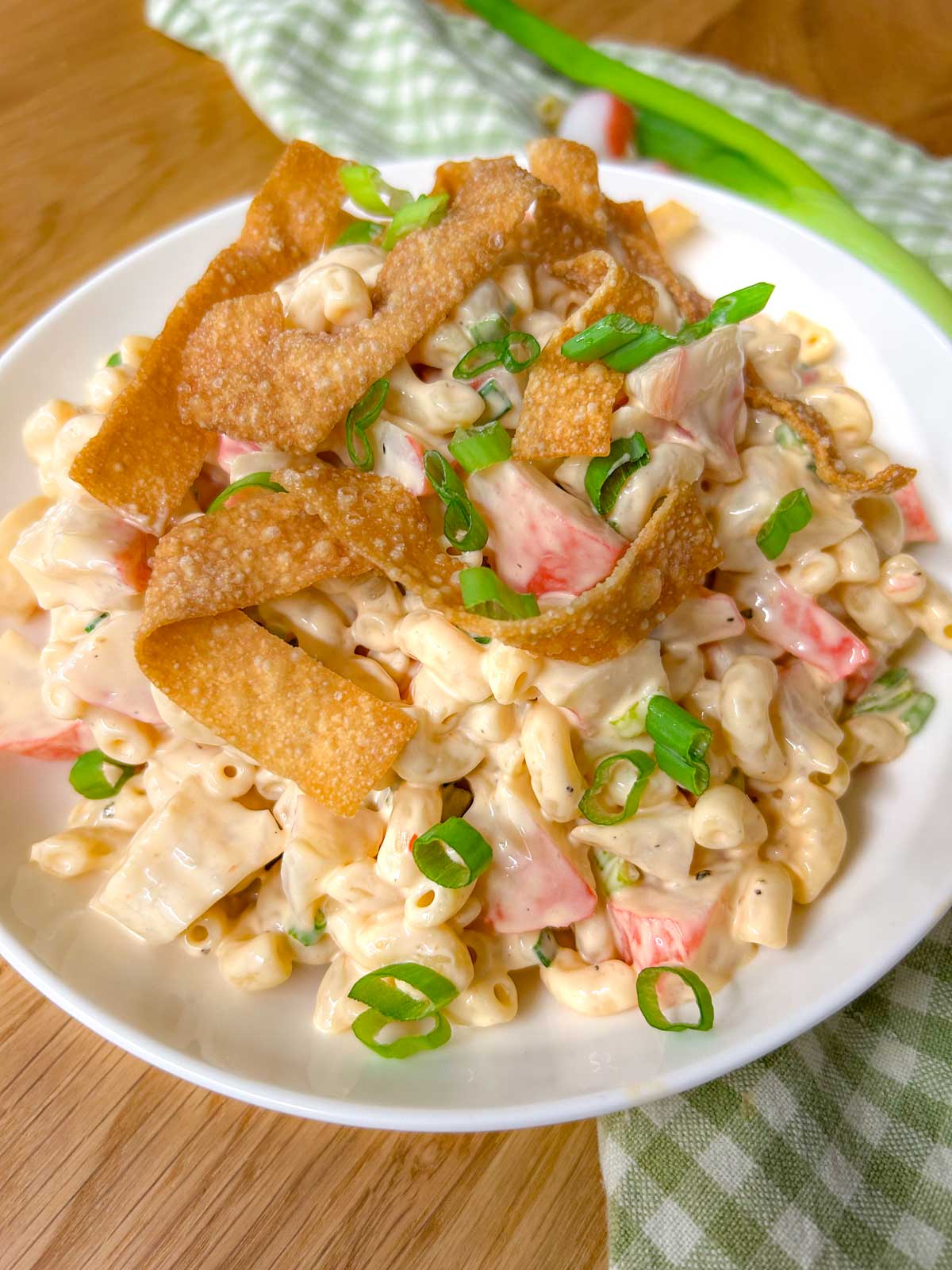 a white bowl is filled with crab rangoon pasta salad topped with crispy wonton strips and green onions.