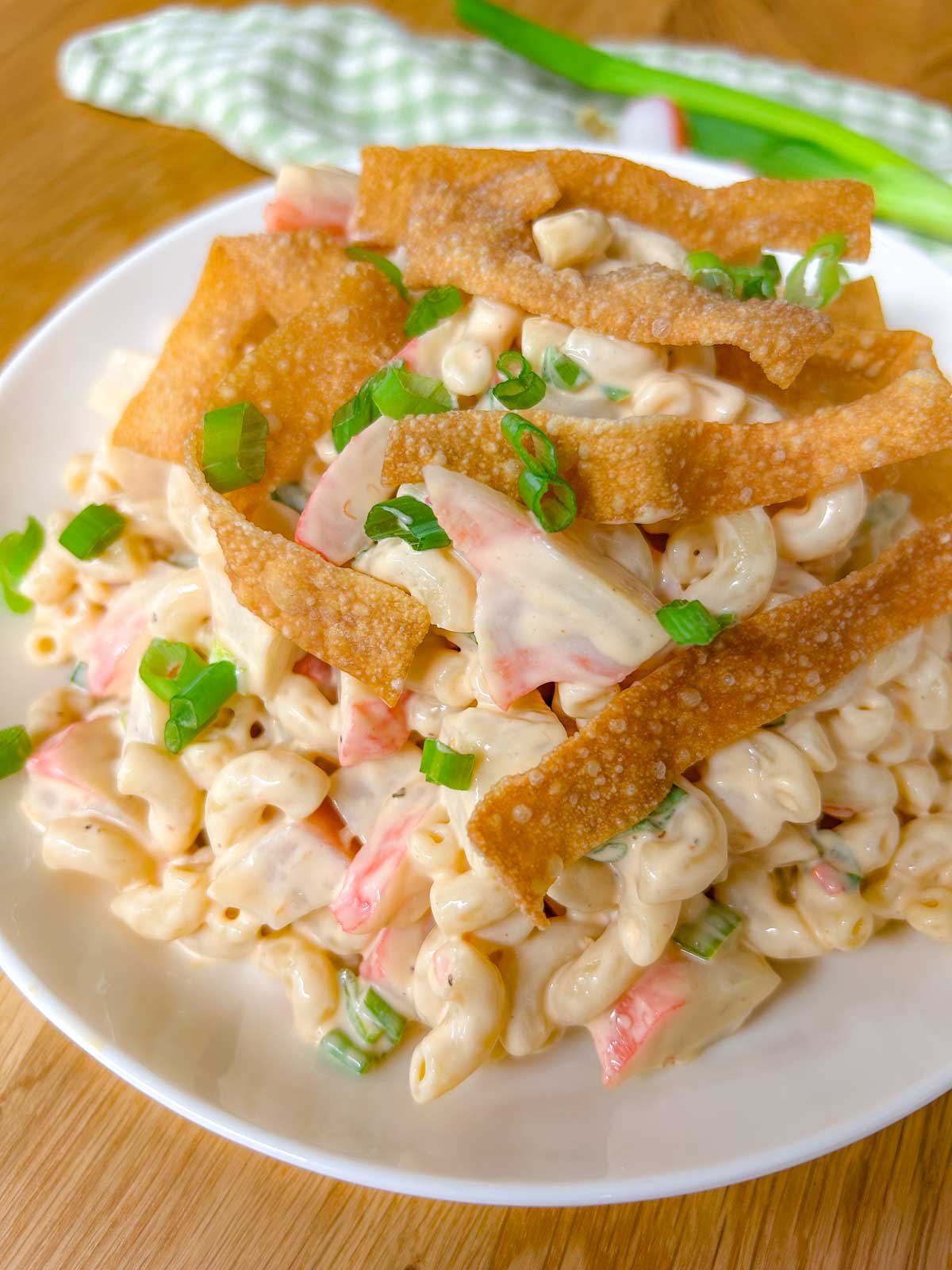 a white bowl is filled with crab rangoon pasta salad topped with crispy wonton strips and green onions.