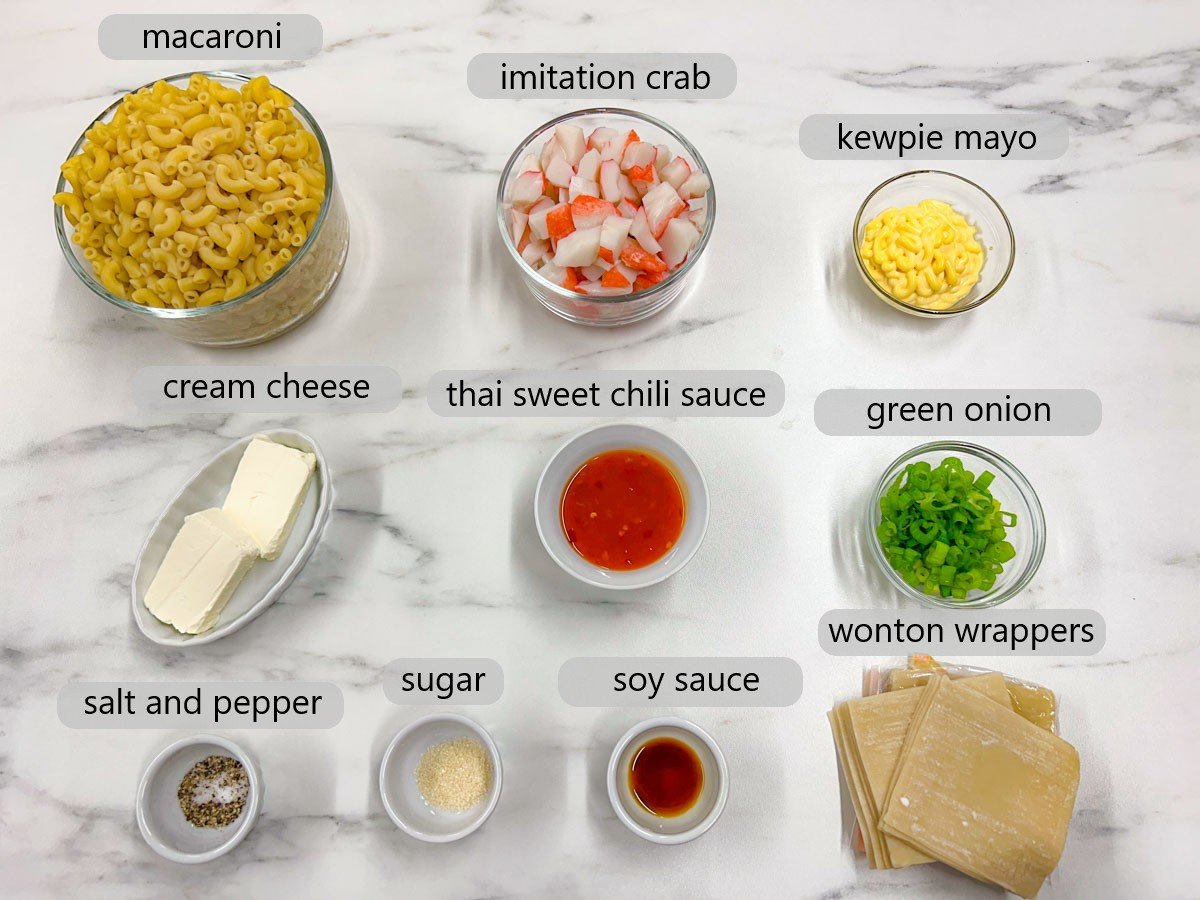 a white marble kitchen counter has bowls with ingredients and text overlay of each reading macaroni, imitation crab, kewpie mayo, cream cheese, Thai sweet chili sauce, green onion, salt and pepper, sugar, soy sauce, and wonton wrappers.
