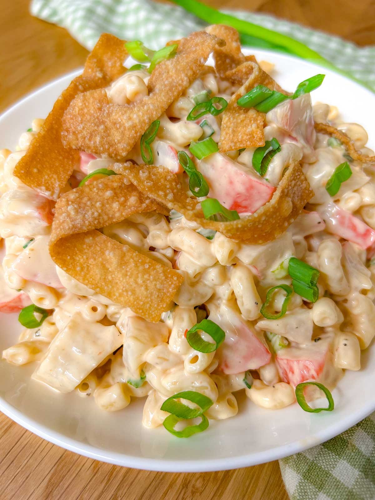 a white bowl is filled with crab rangoon pasta salad topped with crispy wonton strips and green onions.