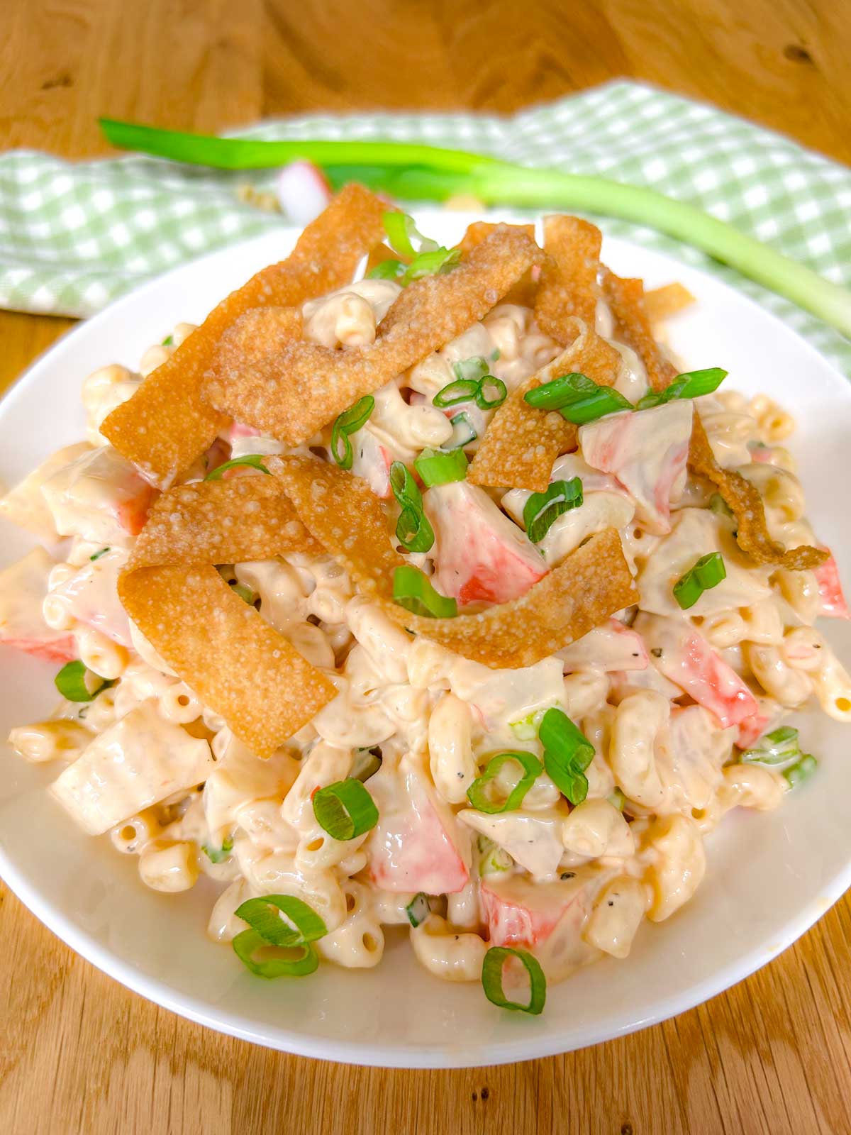 a white bowl is filled with crab rangoon pasta salad topped with crispy wonton strips and green onions.