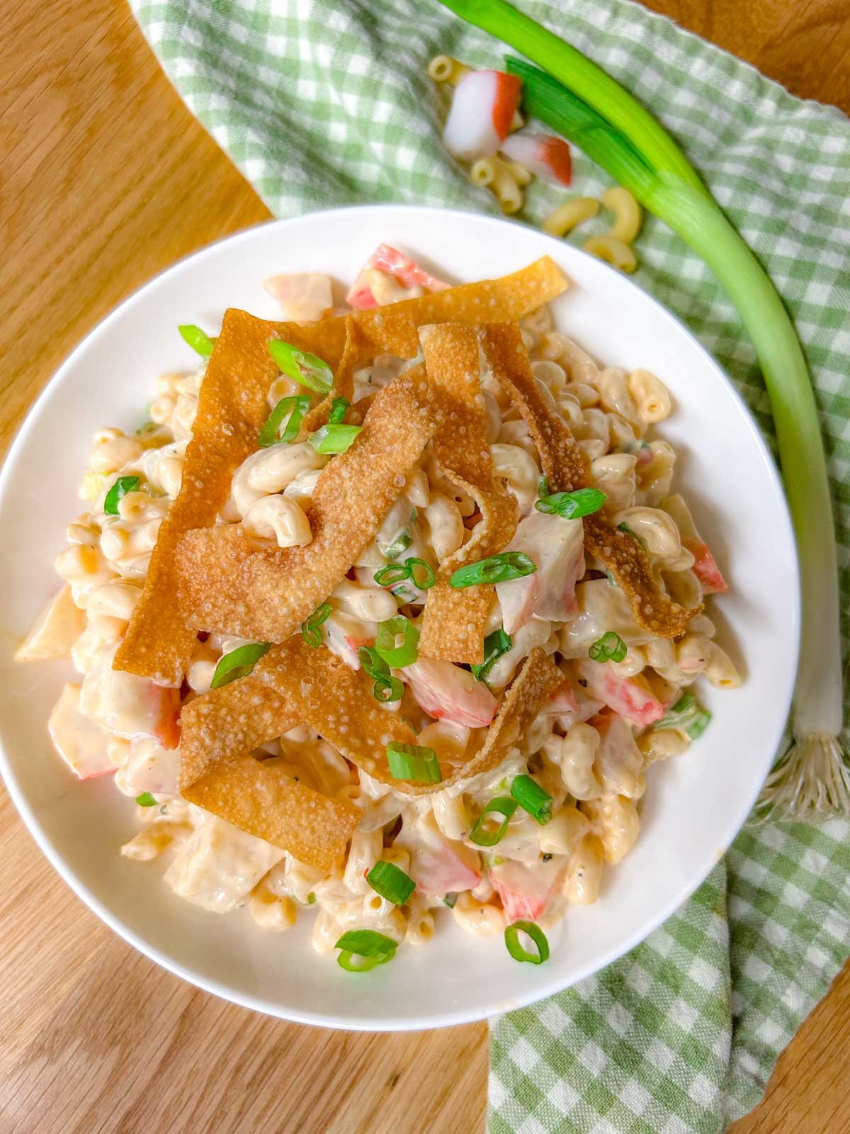 a white bowl is filled with crab rangoon pasta salad topped with crispy wonton strips and green onions.