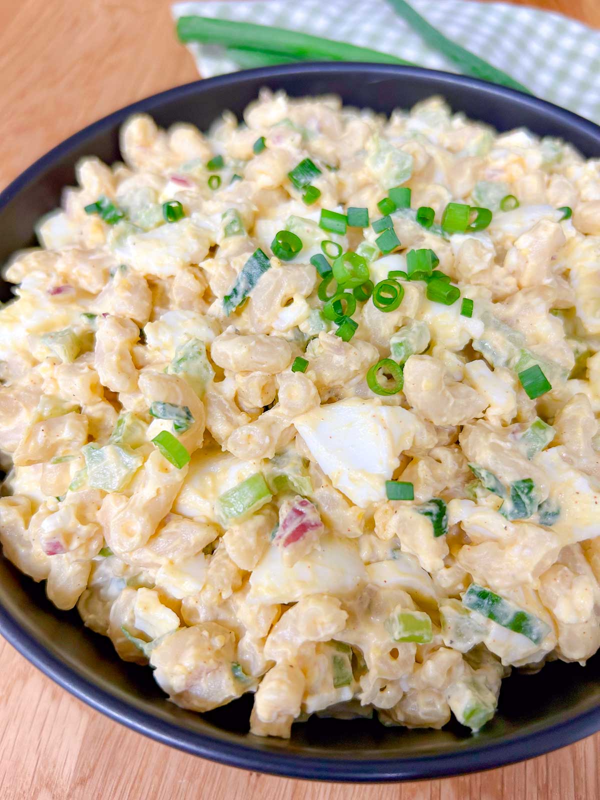 a black bowl is filled with deviled egg pasta salad and garnished with green onions.