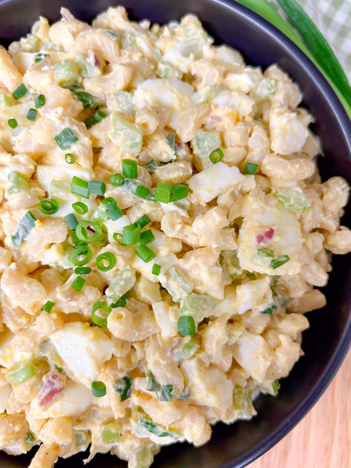 a black bowl is filled with deviled egg pasta salad and garnished with green onions.