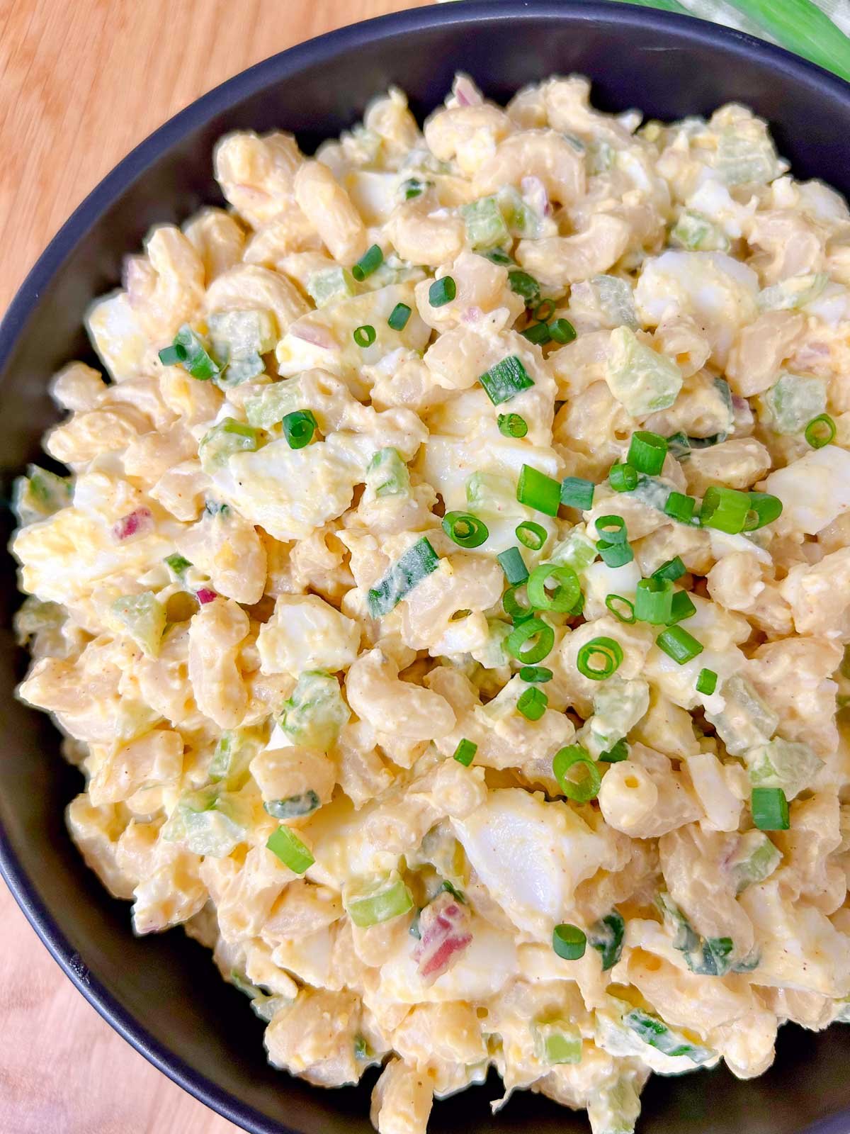 a black bowl is filled with deviled egg pasta salad and garnished with green onions.