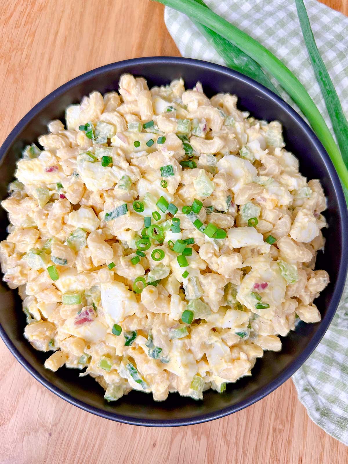 a black bowl is filled with deviled egg pasta salad and garnished with green onions.