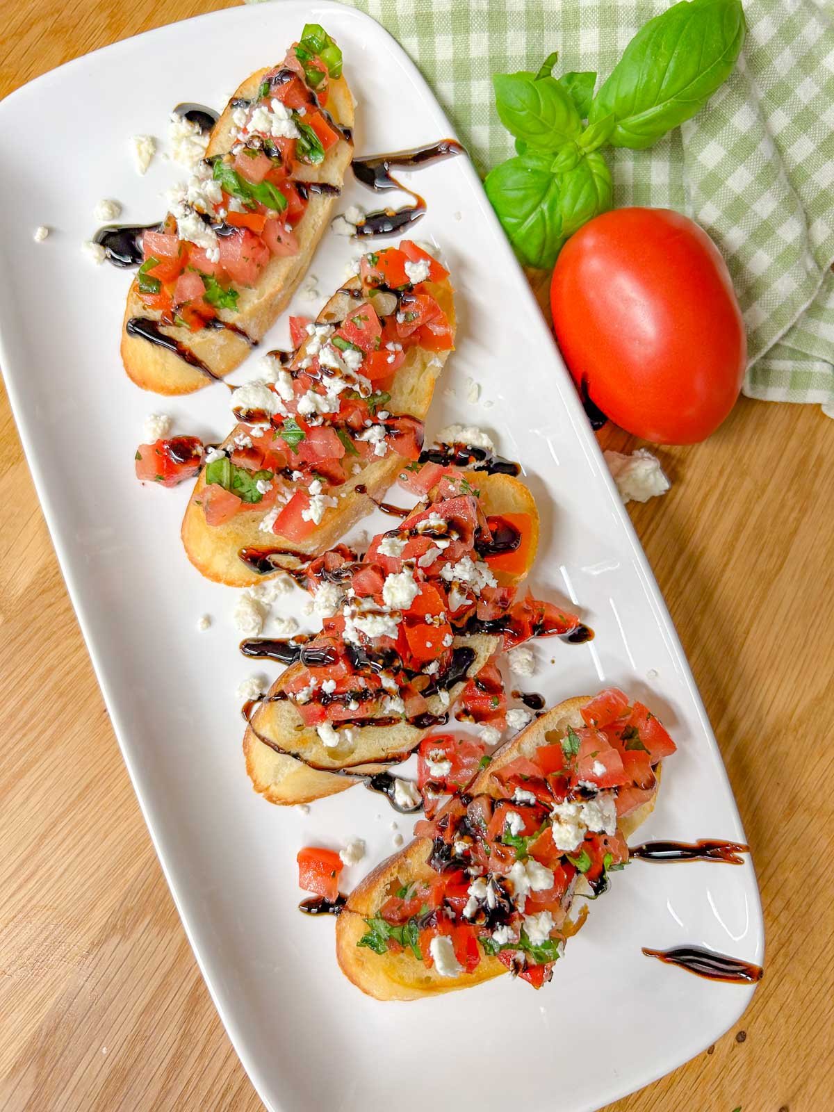 a white serving platter has 4 pieces of bruschetta with crumbled feta cheese and balsamic glaze on top.