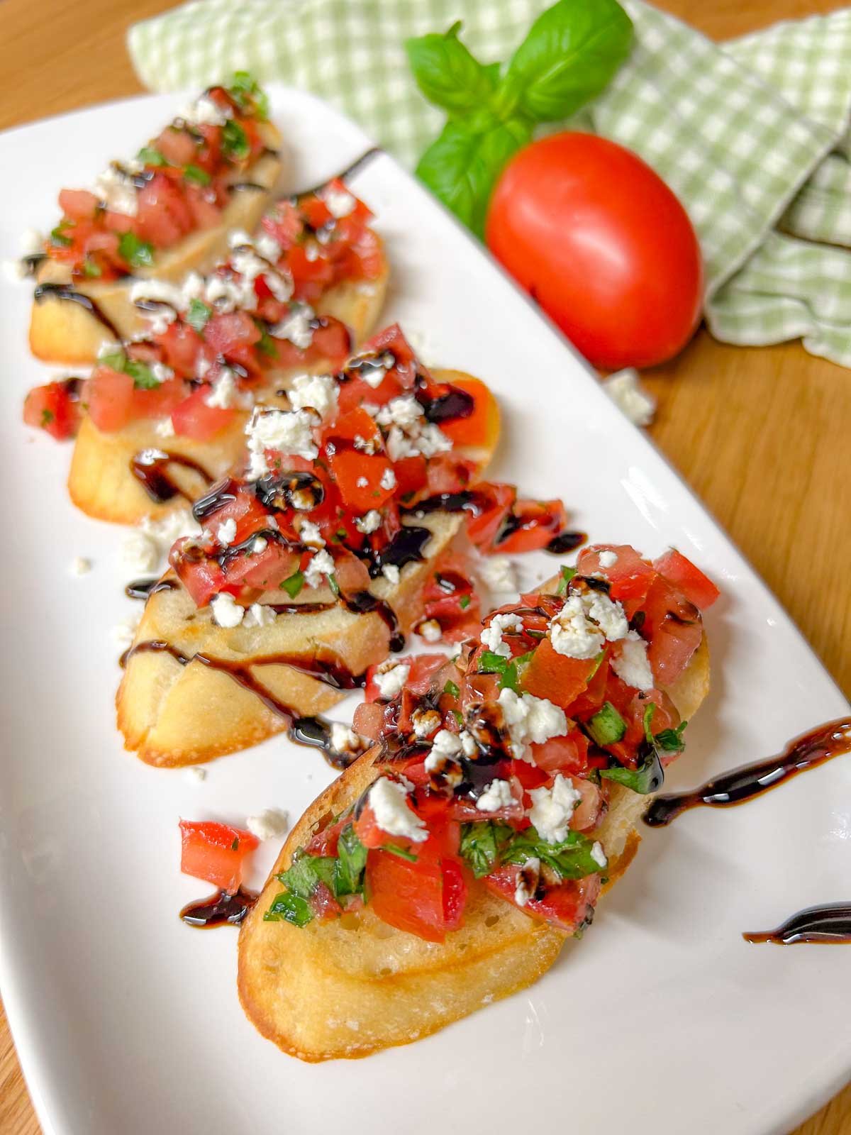 a white serving platter has 4 pieces of bruschetta with crumbled feta cheese and balsamic glaze on top.