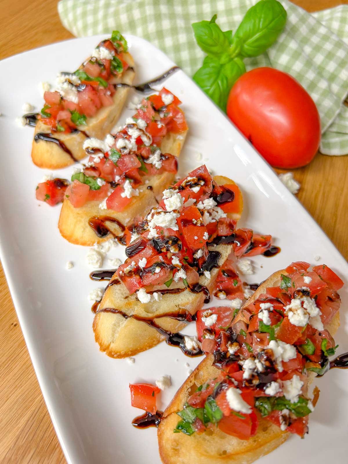 a white serving platter has 4 pieces of bruschetta with crumbled feta cheese and balsamic glaze on top.