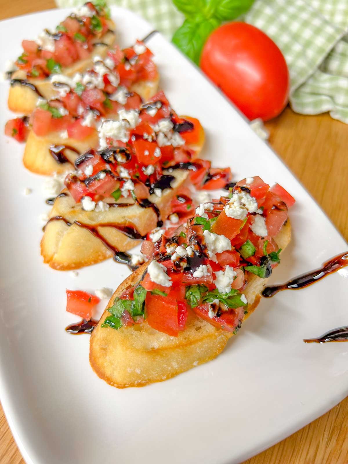 a white serving platter has 4 pieces of bruschetta with crumbled feta cheese and balsamic glaze on top.
