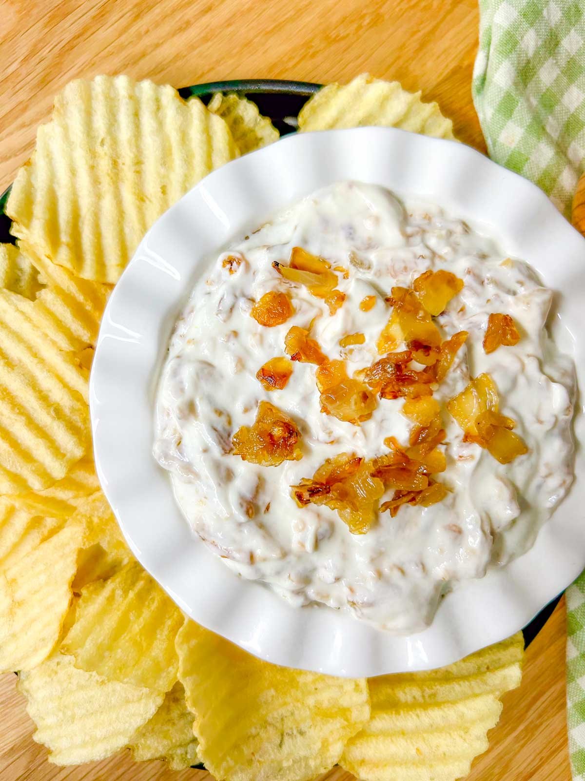 a white bowl is filled with French onion dip and garnished with caramelized onions.