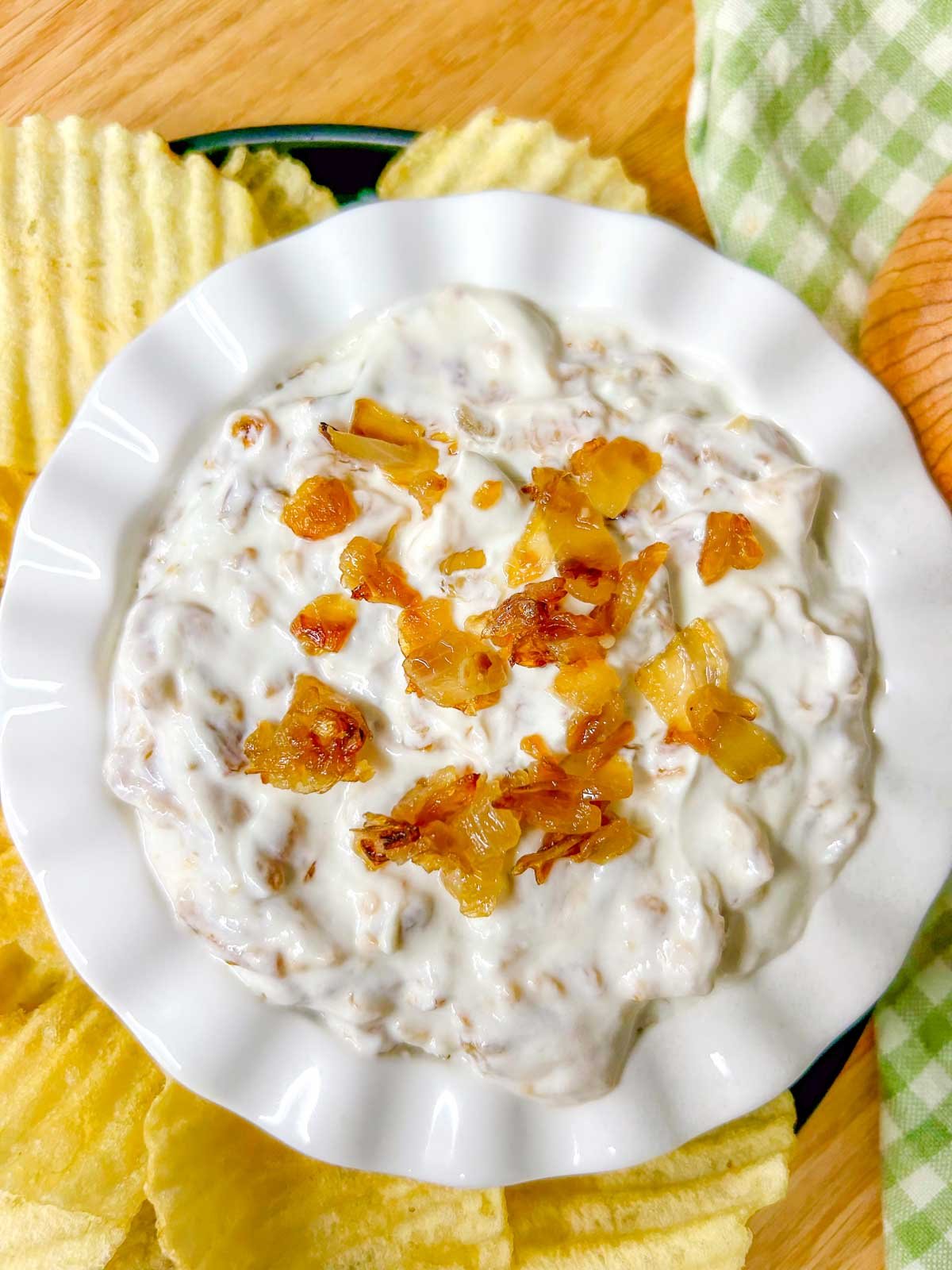 a white bowl is filled with French onion dip and garnished with caramelized onions.