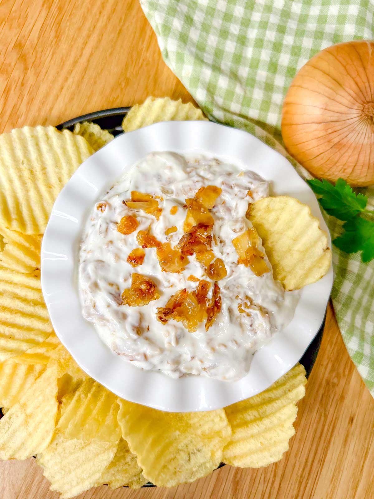 a white bowl is filled with French onion dip and garnished with caramelized onions. a chip is placed in the dip.