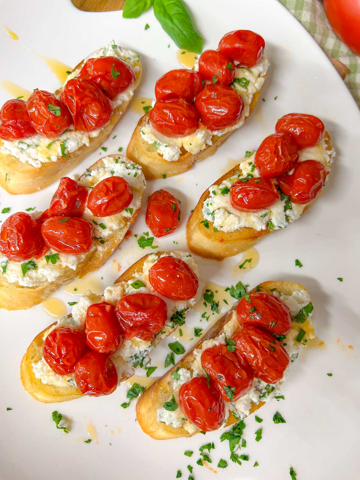 a white serving platter has pieces of hot honey roasted bruschetta on top and is garnished with hot honey, basil, and parsley.