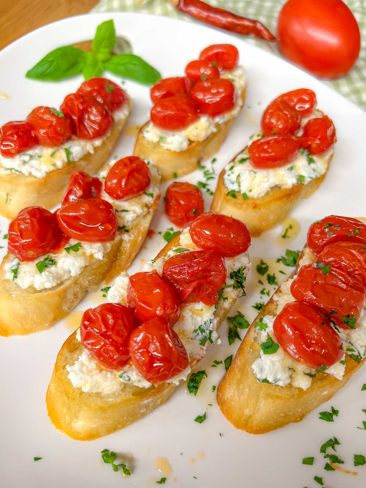 a white serving platter has pieces of hot honey roasted bruschetta on top and is garnished with hot honey, basil, and parsley.