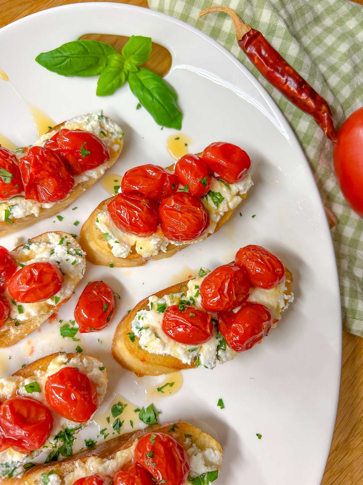 a white serving platter has pieces of hot honey roasted bruschetta on top and is garnished with hot honey, basil, and parsley.