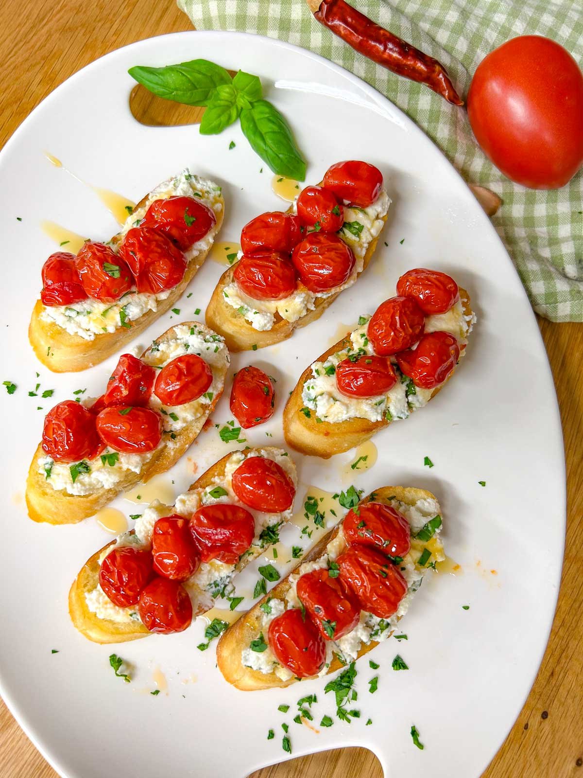 a white serving platter has pieces of hot honey roasted bruschetta on top and is garnished with hot honey, basil, and parsley.