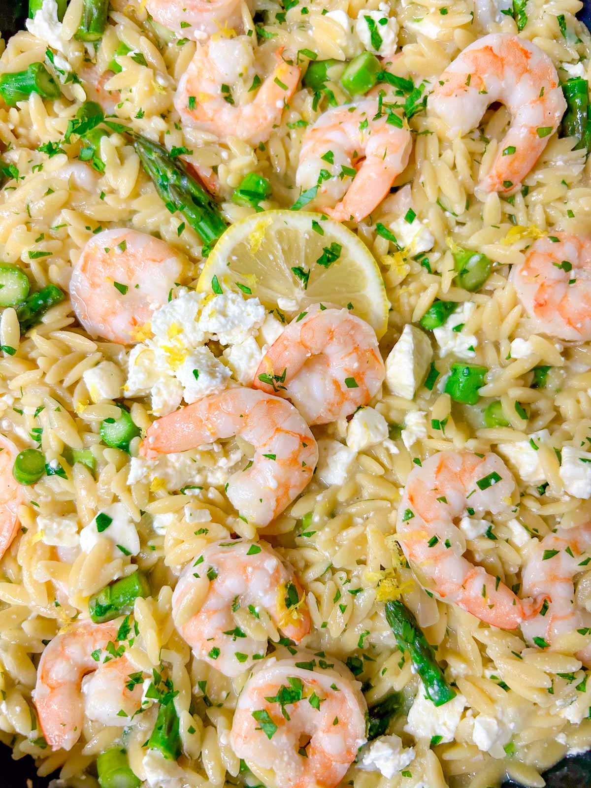 a black frying pan is filled with lemon feta shrimp orzo and garnished with parsley