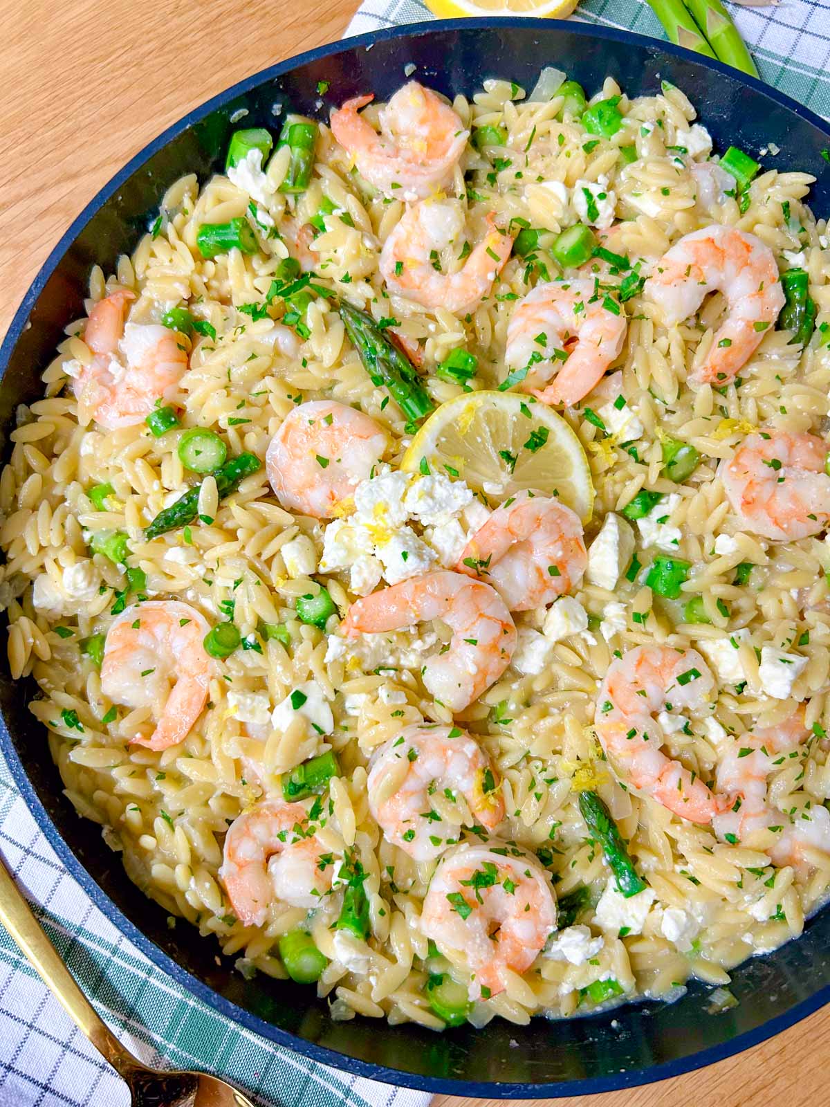 a black frying pan is filled with lemon feta shrimp orzo and garnished with parsley