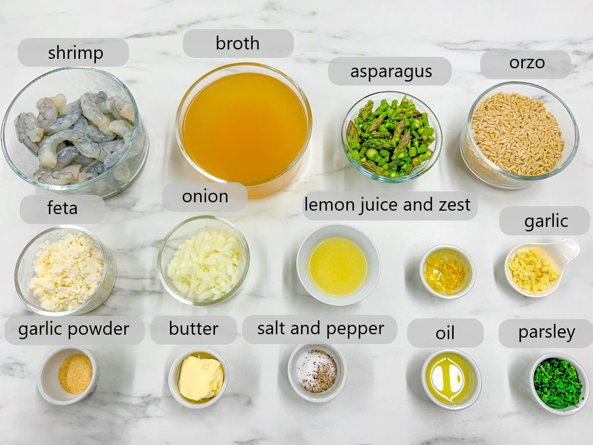 a white marble counter top has bowls with the ingredients to make lemon feta shrimp orzo with labels - shrimp, broth, asparagus, orzo, feta, onion, lemon juice and zest, garlic, garlic powder, butter, salt and pepper, oil, parsley.