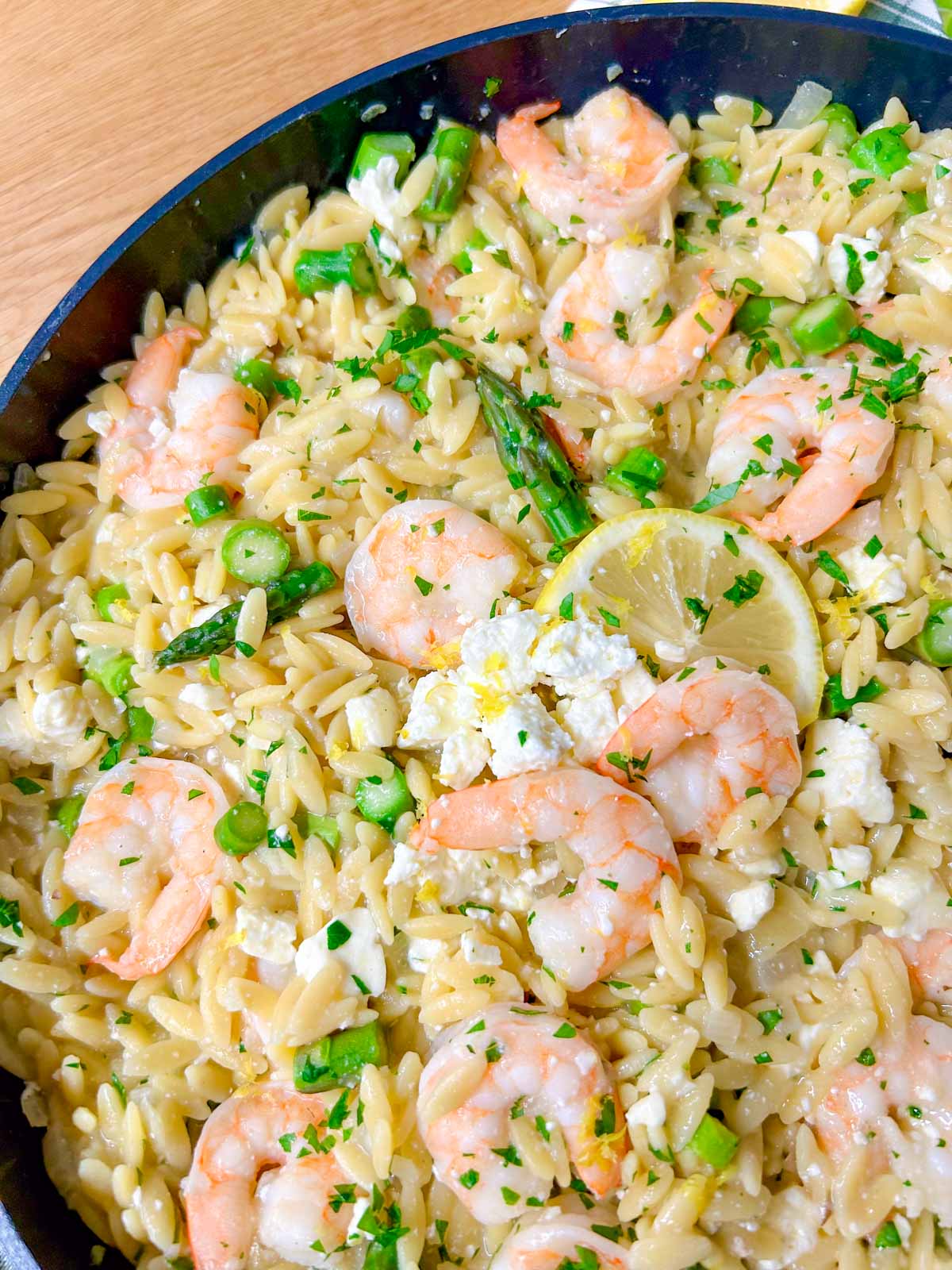 a black frying pan is filled with lemon feta shrimp orzo and garnished with parsley