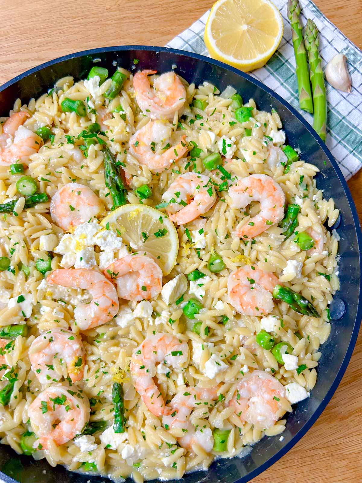 a black frying pan is filled with lemon feta shrimp orzo and garnished with parsley