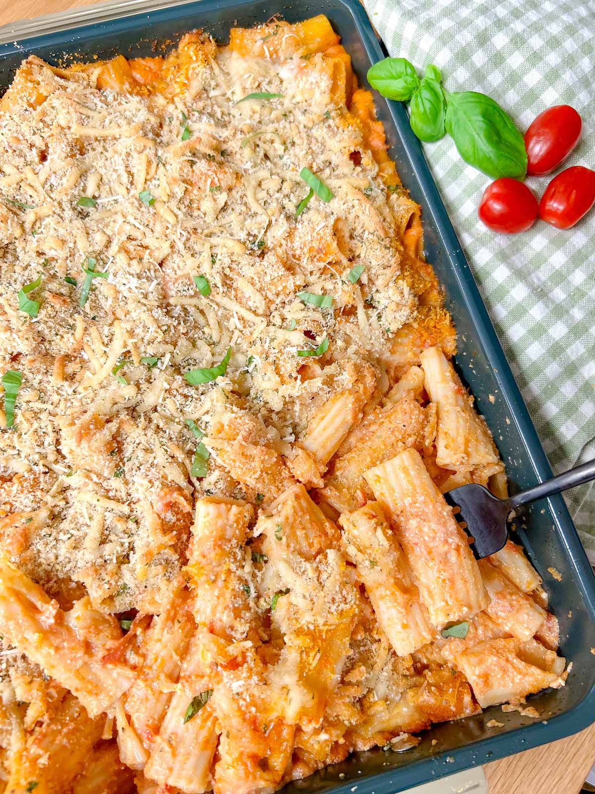 a baking tray has a five cheese ziti al forno baked into it and garnished with fresh basil.