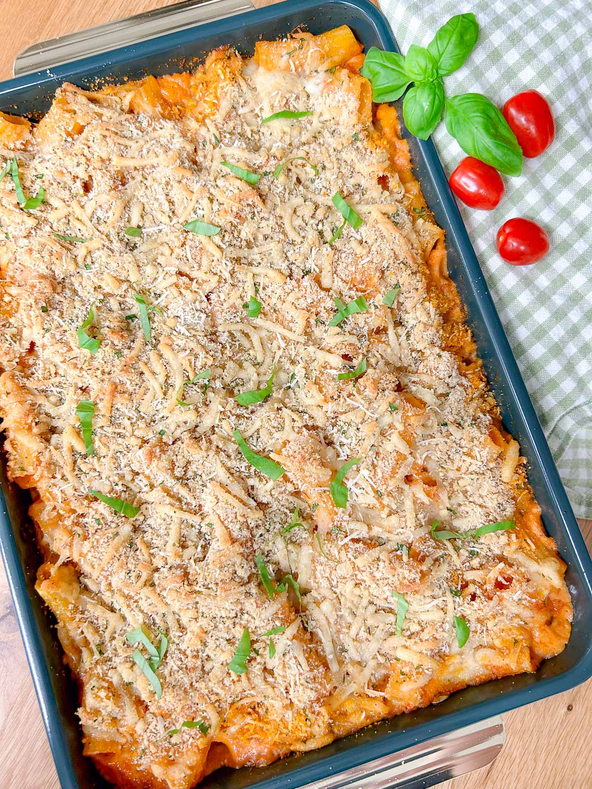 a baking tray has a five cheese ziti al forno baked into it and garnished with fresh basil.
