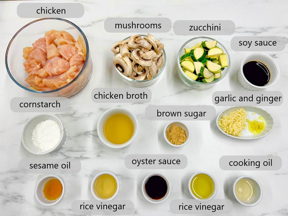 a white marble kitchen counter has bowls with the ingredients to make panda express mushroom chicken copycat with labels reading - chicken, mushrooms, zucchini, soy sauce, cornstarch, chicken broth, brown sugar, garlic, ginger, sesame oil, rice vinegar, oyster sauce, and cooking oil