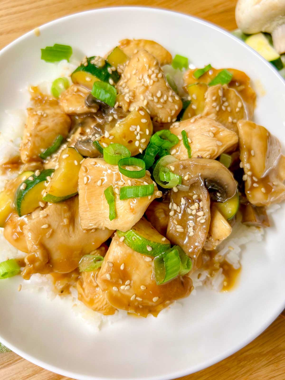 a white bowl is filled with Panda Express mushroom chicken copycat and garnished with sesame seeds and green onions