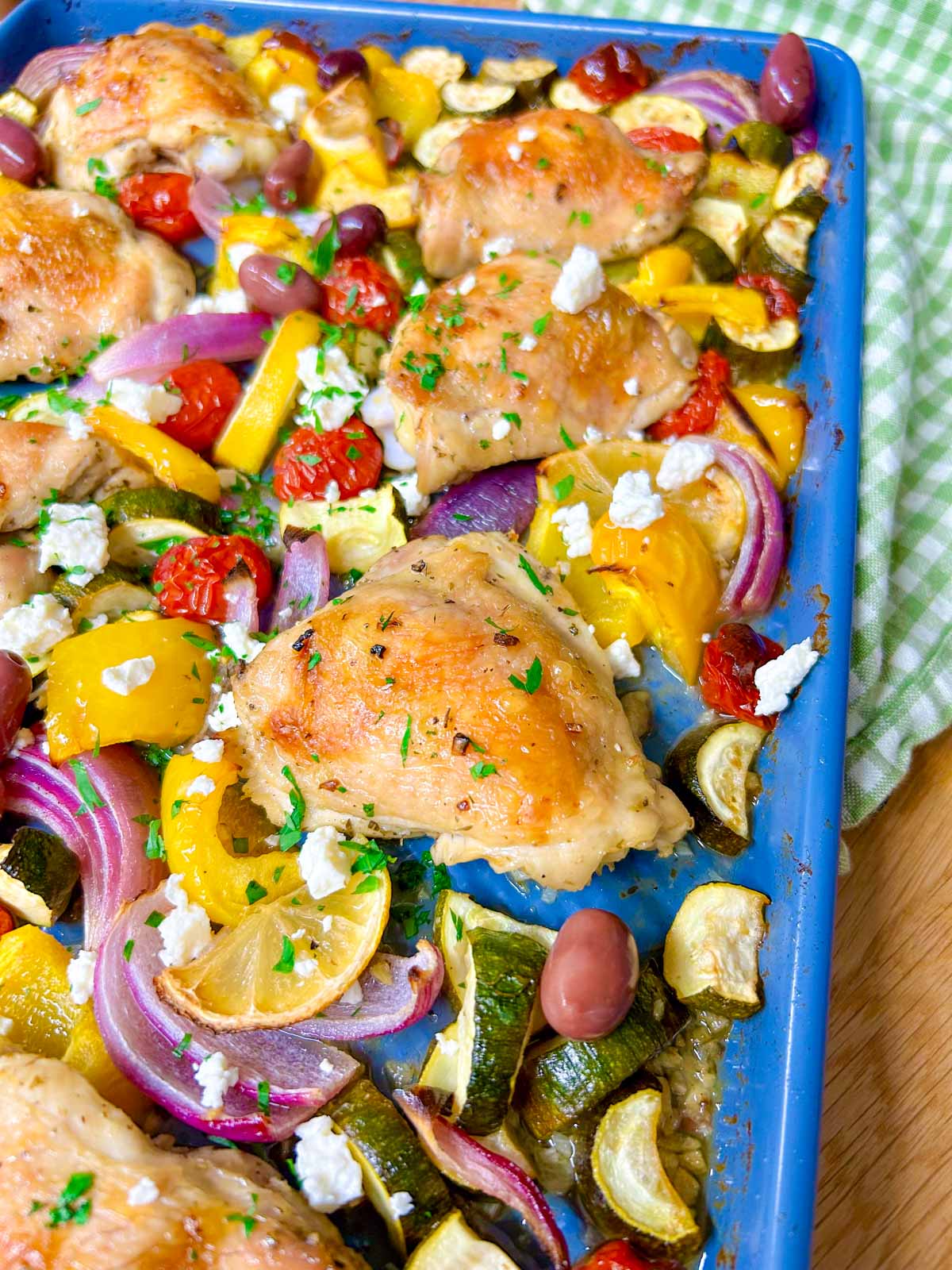 a greek sheet pan dinner is on a sheet pan with chicken thighs, roasted vegetables and feta cheese